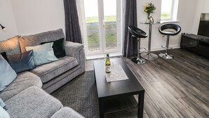A modern living room with a grey sofa, a coffee table, a TV, and a balcony with a view.