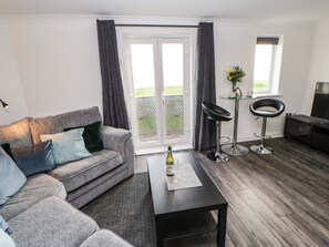 A modern living room with a grey sofa, a coffee table, a TV, and a balcony with a view. - Sandy Corner (Blyth)