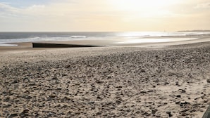 A beach with a rocky foreground and a wooden pier extending into the water.