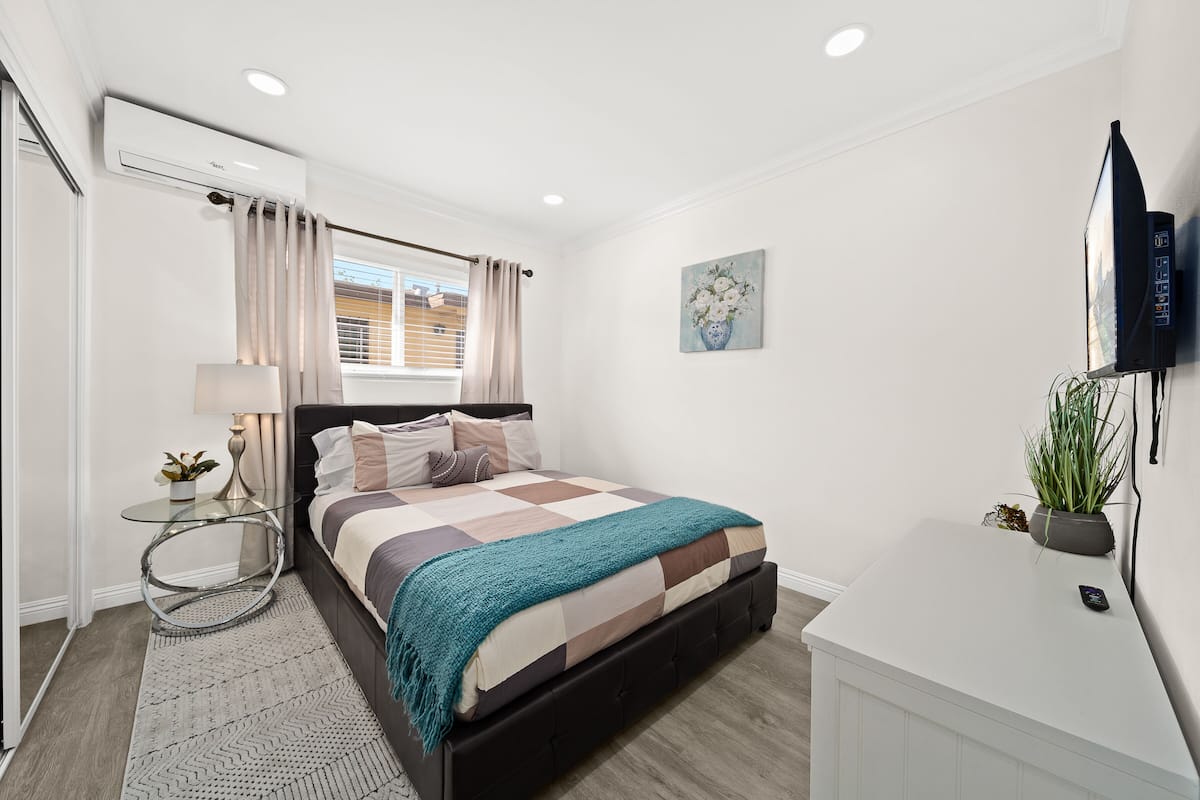 A modern bedroom with a bed, bedside table, lamp, and a mounted TV.