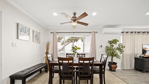 Un comedor con ventilador de techo, un banco, una mesa con sillas y plantas en macetas.