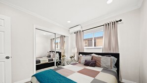 Un dormitorio con cama, espejo, ventana con cortinas y equipo de aire acondicionado.