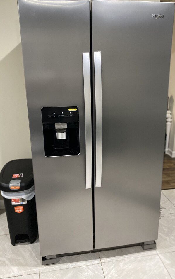 Een roestvrijstalen Whirlpool koelkast met een waterdispenser en een prullenbak ernaast.