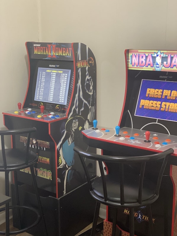 Deux bornes d’arcade, l’une portant l’inscription « Midway Mortal Kombat » et l’autre « NBA Jam », avec des sièges devant.