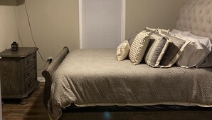 A bedroom with a bed, a ceiling fan, a TV mounted on the wall, and a wooden dresser.
