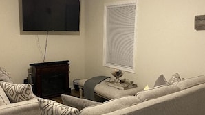 A living room with a ceiling fan, a flat-screen TV, a fireplace, and a window with blinds.