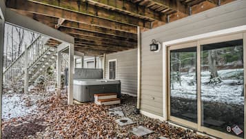 A covered outdoor area with a hot tub, a staircase, and a large window with a view of a snowy landscape.