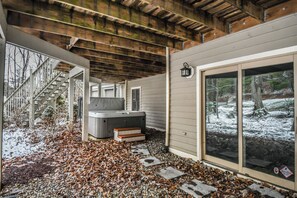 A covered outdoor area with a hot tub, a staircase, and a large window with a view of a snowy landscape. - Black Bear Lodge by Taylor Made Deep Creek (Oakland)