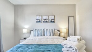 A neatly made bed with a blue blanket, two bedside lamps, and a stack of white towels. - 3bdfamily Retreat Near COS Airport & Fort Carson (Colorado Springs)