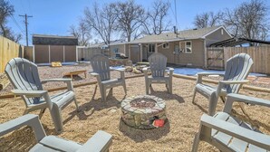 A backyard with Adirondack chairs, a stone fire pit, and a house with a covered patio. - 3bdfamily Retreat Near COS Airport & Fort Carson (Colorado Springs)