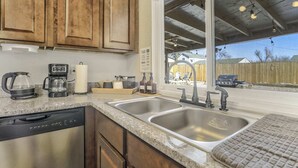 A kitchen with wooden cabinets, a dishwasher, a coffee maker, and a sink. - 3bdfamily Retreat Near COS Airport & Fort Carson (Colorado Springs)