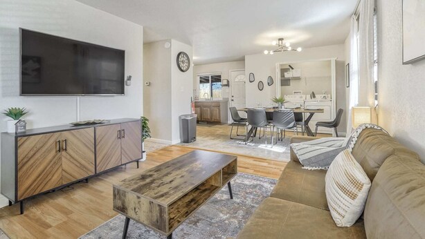 A modern living room with a sofa, coffee table, and TV. There is a dining area with chairs and a table, and a kitchen in the background. - 3bdfamily Retreat Near COS Airport & Fort Carson (Colorado Springs)