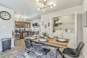 A compact kitchen with modern appliances, a dining area with a wooden table and chairs, and a visible fire extinguisher. - 3bdfamily Retreat Near COS Airport & Fort Carson (Colorado Springs)