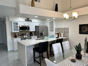 A modern kitchen with white cabinetry, stainless steel appliances, and a central island with bar stools. - Elegant and luxurious Apartment near Disney (Kissimmee)