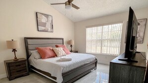 Ein Schlafzimmer mit einem Bett, Nachttischen, einem Deckenventilator, einem Fenster und einem Fernseher.