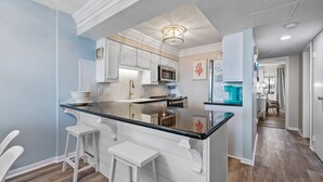 A modern kitchen with white cabinetry, a black countertop, and a bar stool. - Direct Oceanfront! Renovated! All beach gear included (North Myrtle Beach)