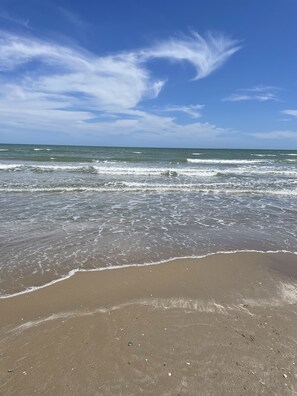 A beach with waves approaching the shore under a clear sky.