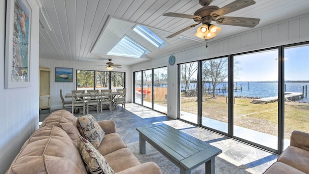 A spacious living area with a large window overlooking a body of water, a ceiling fan, and a dining area with a table and chairs. - Updated Waterfront Escape w/ Dock & Fire Pit (Pensacola)