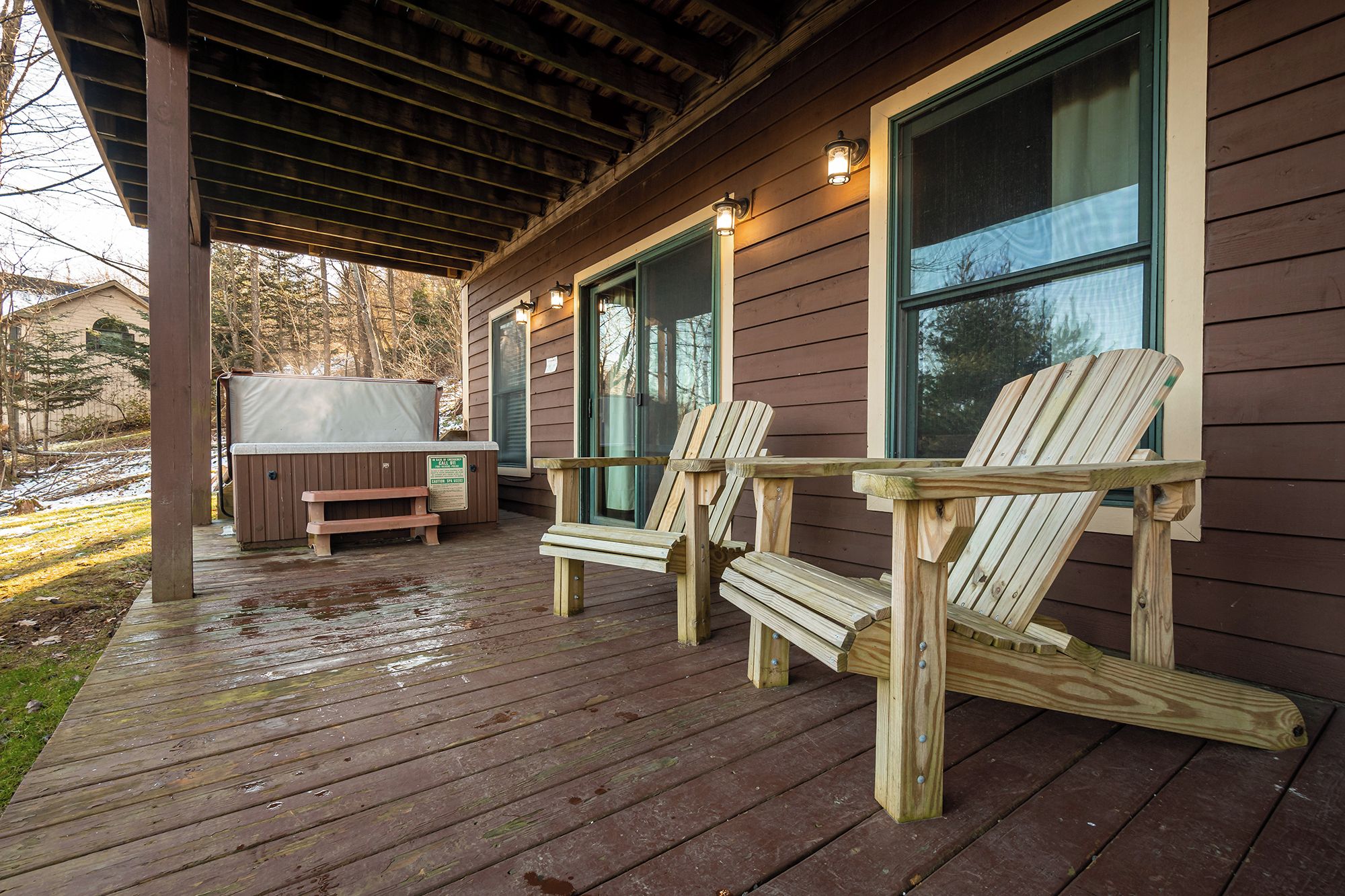 Eine Holzterrasse mit zwei Adirondack-Stühlen, einem Whirlpool und einem überdachten Balkon.