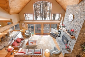 Relax in this spacious living area with a high ceiling, featuring a large skylight, comfortable seating, and a stone fireplace.