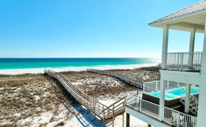 A beach view with a wooden boardwalk leading to a white building with a pool. - Sanctuary at Navarre Beach - 8 BR/8 BA Beach House w/pool. (Navarre Beach)
