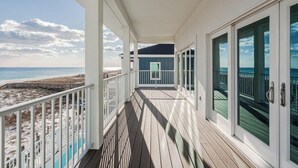 Une terrasse en bois avec des portes vitrées donnant sur un balcon qui offre une vue sur la plage.