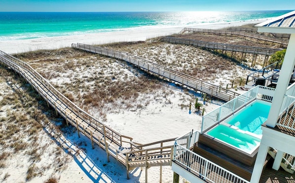Un complejo turístico frente a la playa con piscina, pasarelas de madera y vistas al océano.
