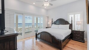 Une chambre à coucher comprenant un lit, un ventilateur de plafond, une table de chevet, une commode et une vue sur l’océan grâce à de grandes fenêtres.