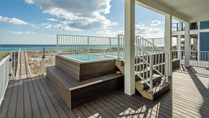 Une terrasse en bois avec un jacuzzi et un escalier menant à un balcon donnant sur la plage.
