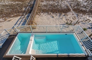 Una piscina en la azotea con cubierta de madera y barandales de metal, rodeada de terreno arenoso.