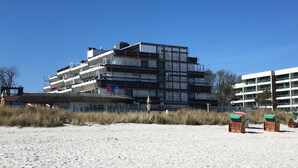 A multi-story building with a modern architectural design, located adjacent to a sandy beach. - Ter/215 - Terrassenhuegel - Seeblick (Scharbeutz)