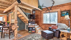 Ein rustikales Blockhaus mit einer Holztreppe, einem Kamin, einem Fernseher und einer gemütlichen Sitzecke.