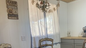 A rustic cabin interior with a wooden dining table surrounded by four chairs, a chandelier, and a kitchen area with a coffee maker. - The Cozy Cottage (Toccoa)