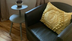 A room with a black leather armchair, a small round table with a decorative item, and a window with curtains. - The Cozy Cottage (Toccoa)