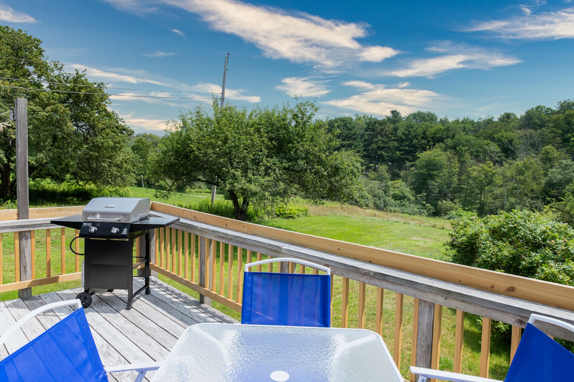Une terrasse avec un barbecue, une chaise bleue et une vue sur un paysage verdoyant.