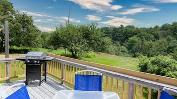 Une terrasse avec un barbecue, une chaise bleue et une vue sur un paysage verdoyant.