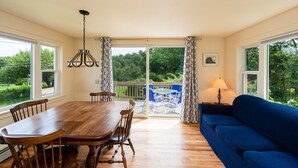 A dining area with a wooden table and chairs, a blue sofa, and a view of greenery through large windows.