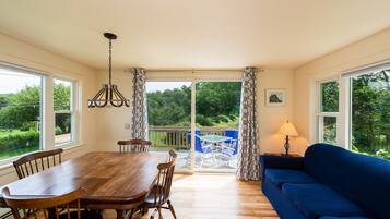 Un coin repas avec une table et des chaises en bois, un canapé bleu et une vue sur la verdure grâce à de grandes fenêtres.