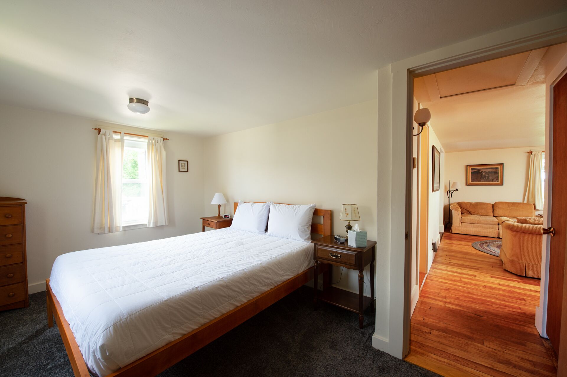 Une chambre avec un grand lit, une table de chevet avec une lampe, une commode et une fenêtre avec des rideaux.