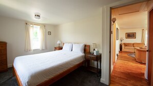 A bedroom with a large bed, a nightstand with a lamp, a dresser, and a window with curtains.