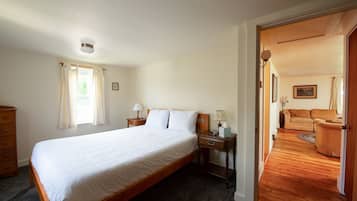 Une chambre avec un grand lit, une table de chevet avec une lampe, une commode et une fenêtre avec des rideaux.