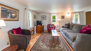 A living room with a sofa, armchairs, a coffee table, a television, and a rug.