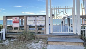 A wooden gate with a 'NO PARKING TOW AWAY ZONE' sign, a beach retreat sign, and a private beach resort sign.