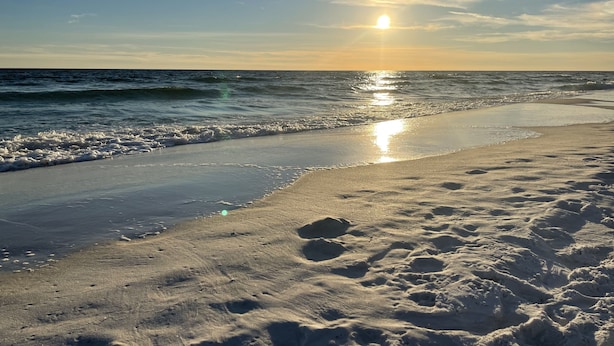 A beach with footprints in the sand and waves approaching the shore.