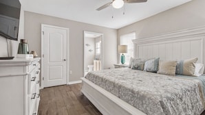 A bedroom with a large bed, a ceiling fan, a dresser, and a mirror.