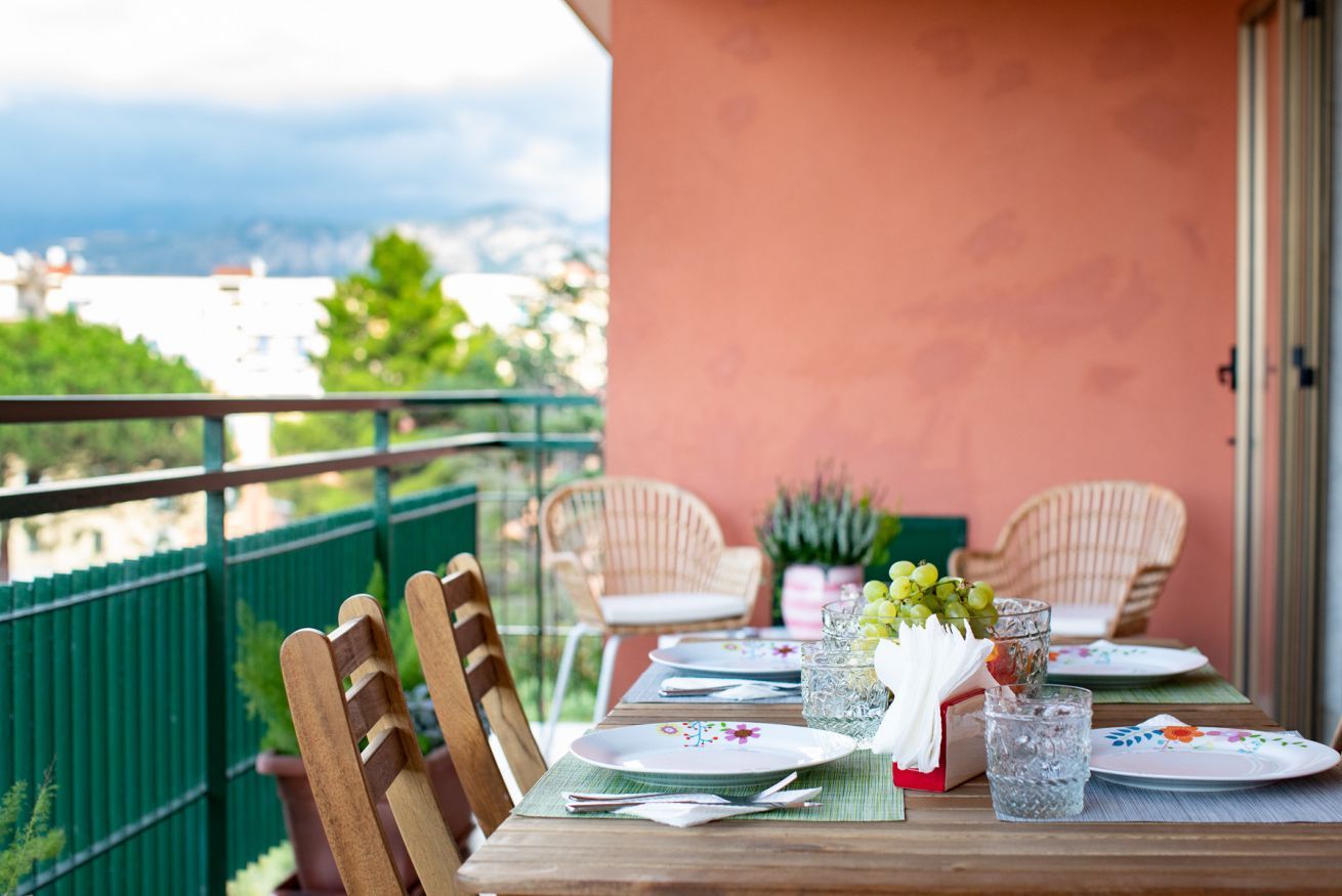 A dining table set for two with chairs, a view of the city, and a balcony railing.
