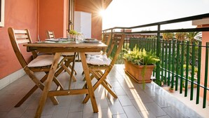Un balcón con mesa y sillas de madera, plantas en macetas y vistas del entorno.