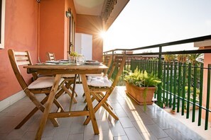 A balcony with a wooden table and chairs, potted plants, and a view of the surrounding area.