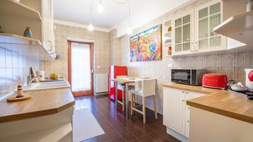 A modern kitchen with white cabinets, a red toaster, and a colorful painting on the wall.