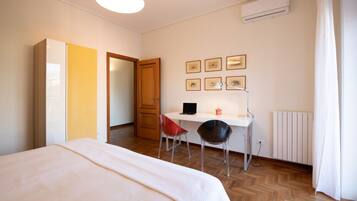 A bedroom with a bed, a desk with a chair, a radiator, and framed pictures on the wall.